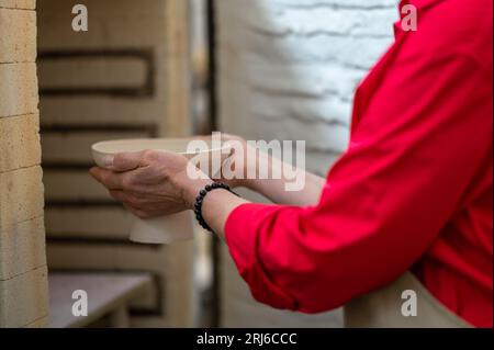 Artigiana che colloca tazze di argilla nel forno per cuocere la ceramica mentre lavora in officina. Foto Stock