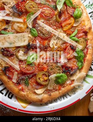 Una pizza appena sfornata con una varietà di condimenti disposti su un piatto bianco sporco Foto Stock