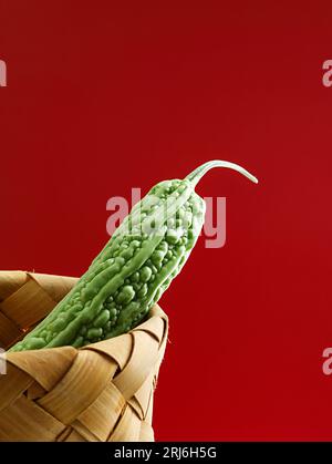 Immagine ravvicinata di tre meloni amari verdi maturi in un cestino di vimini su sfondo rosso Foto Stock