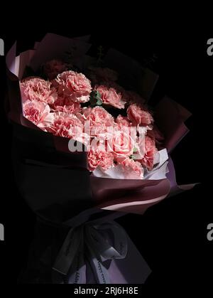 Un bouquet vibrante di garofani rosa e bianco e rose disposti su un colore nero Foto Stock