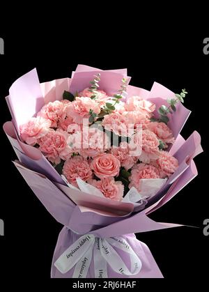 Un bouquet vibrante di garofani rosa e bianco e rose disposti su un colore nero Foto Stock