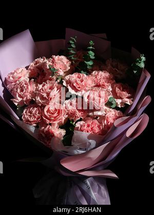 Un bouquet vibrante di garofani rosa e bianco e rose disposti su un colore nero Foto Stock