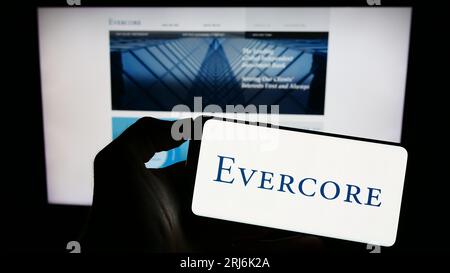 Persona che possiede un telefono cellulare con il logo della società americana di investment banking Evercore Inc. Sullo schermo davanti alla pagina Web. Concentrarsi sul display del telefono. Foto Stock