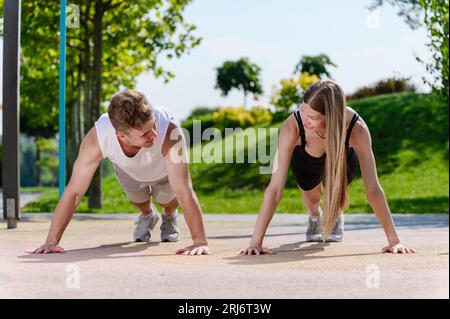 Giovani e graziose coppie che fanno push-up sul campo sportivo all'aperto nel parco cittadino. Foto Stock