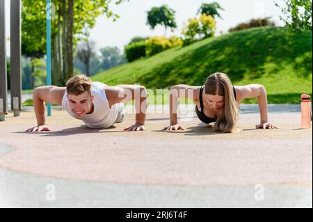 Giovani e graziose coppie che fanno push-up sul campo sportivo all'aperto nel parco cittadino. Foto Stock