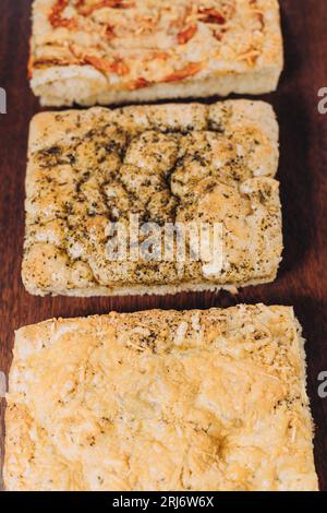 Tre pizze appena preparate con formaggio fuso e varie erbe e spezie sono disposte con cura su un tagliere di legno Foto Stock