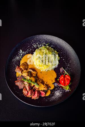 Primo piano di un piatto con un piatto saporito di carne alla griglia servito con riso e condito con una salsa saporita, su sfondo nero Foto Stock