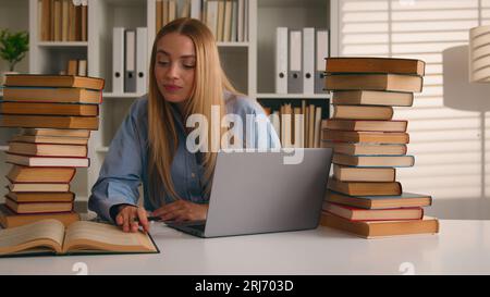 Studentessa caucasica felice ragazza sorridente donna che studia con laptop e libri compiti imparare la conoscenza online preparare per esame di prova studio in biblioteca Foto Stock