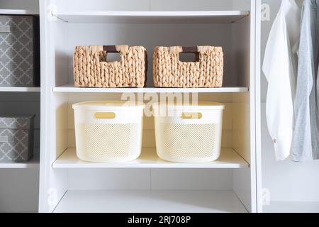 Un armadio bianco con più cestini sugli scaffali e diversi capi di abbigliamento appesi all'asta dell'armadio Foto Stock