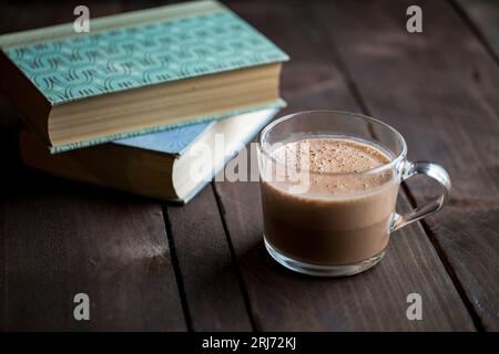 Una tazza di cioccolata calda su un tavolo di legno accanto ai libri. Foto Stock