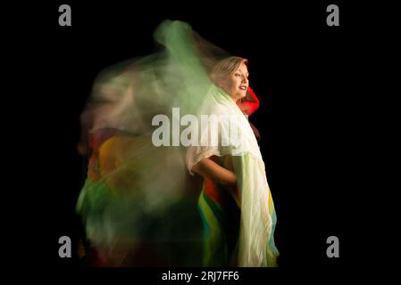 Ritratto in movimento di donna con tessuto verde vestito colorato. Isolato su sfondo nero. Foto Stock