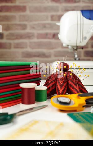 Pila di tessuti rossi e verdi, accessori per cucire e trapuntare e macchina da cucire su sfondo murale Foto Stock