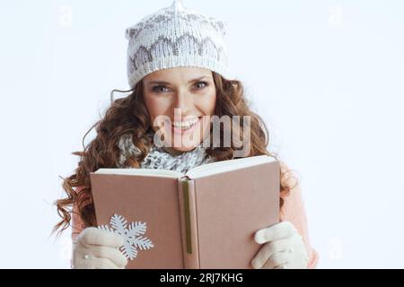 Ciao inverno. donna sorridente di 40 anni con maglione, guanti, cappello e sciarpa su sfondo bianco con fiocco di neve e libro. Foto Stock