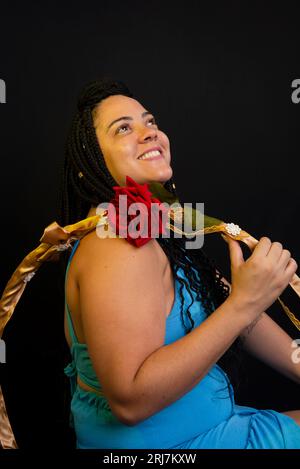 Bella donna che indossa un abito di colore blu seduta con un hula hoop su sfondo nero in studio. Persona positiva. Foto Stock