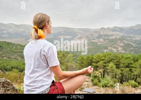 Donna irriconoscibile con smartphone seduto in posa loto yoga Foto Stock