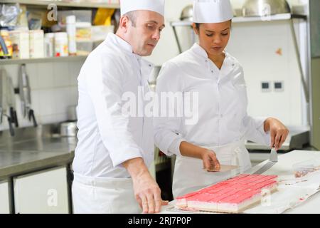 pasticceria e apprendista decorano una torta Foto Stock