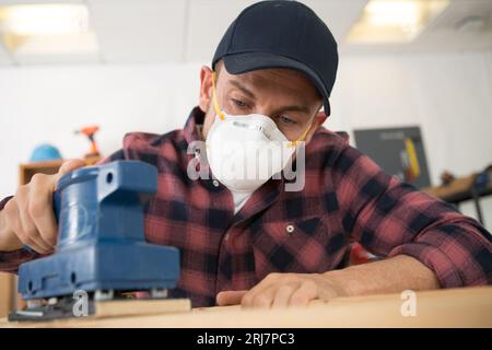 l'uomo lavora con la maschera di sicurezza durante la levigatura del legno Foto Stock