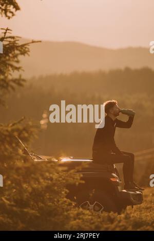 Bel giovane uomo che si rilassa su un cofano di veicolo terreno in campagna Foto Stock