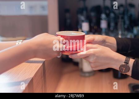 Un bellissimo barista asiatico che consegna una tazza di caffè ai clienti che aspettano gli ordini al bar Foto Stock