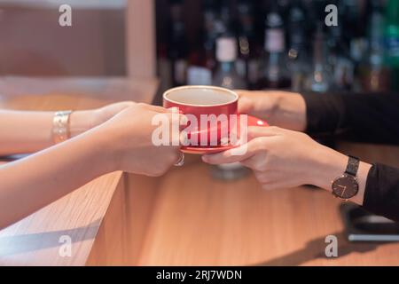 Un bellissimo barista asiatico che consegna una tazza di caffè ai clienti che aspettano gli ordini al bar Foto Stock