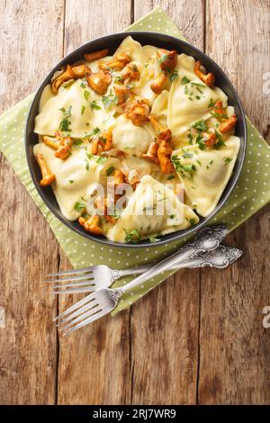 Triangoli è una semplice pasta a forma di triangolo ripiena di funghi chanterelle, cipolla ed erbe sul piatto sul tavolo di legno. Verticale superiore Foto Stock