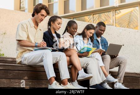 Gruppo multiculturale di studenti seduti nel campus universitario, che si stanno preparando Foto Stock