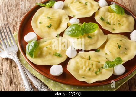 Cappellacci pasta fresca ripiena fatta con una deliziosa mozzarella ripiena e primo piano di basilico sul piatto sul tavolo di legno. Orizzontale Foto Stock