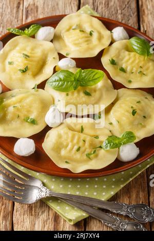 Ravioli cappellacci gnocchi con mozzarella ed erbe in primo piano sul piatto sul tavolo di legno. Verticale Foto Stock