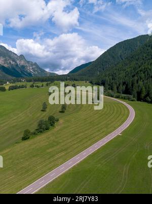 Stretta curva asfaltata nel verde del paesaggio agricolo nella valle di montagna nelle Dolomiti italiane Foto Stock