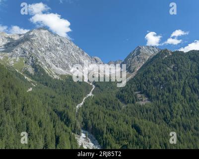 Vette alpine con ruscelli e pini in primo piano sotto il cielo blu. Hochgall del gruppo delle Vedrette di Ries delle Dolomiti in alto Adige Foto Stock