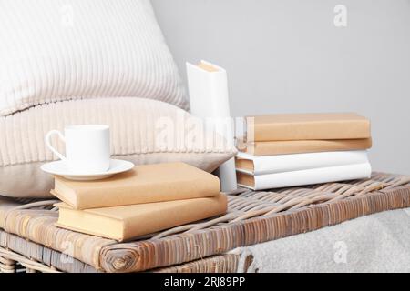 Libri con tazza e cuscini sul cestino vicino a una parete chiara, primo piano Foto Stock