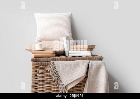 Libri con tazza e cuscini su cestino vicino a una parete luminosa Foto Stock