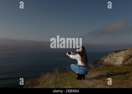 La giovane donna cattura la bellezza costiera attraverso il suo obiettivo mobile Foto Stock