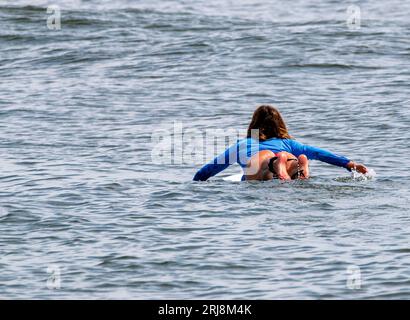 Vista posteriore di una surfista sdraiata sulla sua tavola da surf che nuota fuori per prendere le onde per fare surf a Gilgo Beach Long Island, nell'estate del 2023. Foto Stock