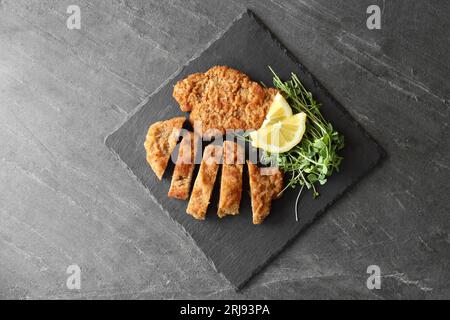 Gustosi schnitzels serviti con microgreen e limone su tavolo grigio, vista dall'alto Foto Stock