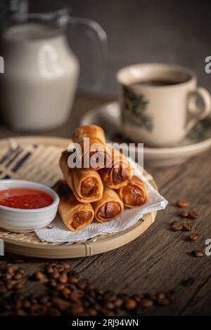 Involtini di primavera fritti su un piatto di rattan con salsa di peperoncino dolce e una tazza di caffè. Spuntini malesi. Colazione malese. Asian Foods. Foto Stock