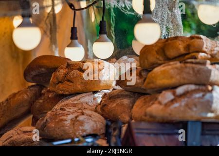Una selezione di pane appena sfornato in esposizione con lampade appese sopra Foto Stock