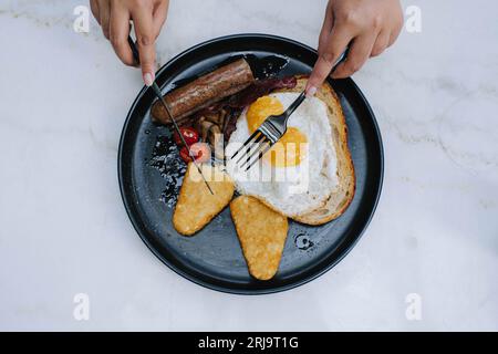 Vista piatta o dall'alto e mirata selezione di mani è affettare l'impasto naturale su un piatto di menu completo inglese per la colazione su un isolato bac bianco Foto Stock