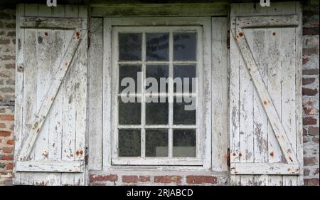 Una vecchia finestra con persiane in legno intemprate. Vista frontale di una finestra con pannelli e di un telaio, usurati e arrugginiti. Foto Stock