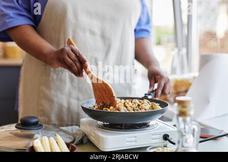 Primo piano della donna nera che frigge verdure in cucina mentre cucina un pasto sano, copia spazio Foto Stock