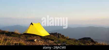 Vista panoramica sulla tenda gialla sullo sfondo del paesaggio montano autunnale durante l'alba mattutina. Montagne sullo sfondo Foto Stock