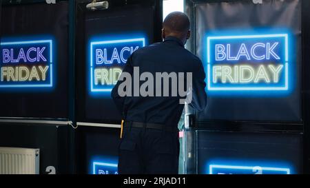 Agente di sicurezza che apre la porta d'ingresso il Black friday, trovando folle folla di clienti aggressivi che cercano di entrare per primi. Clienti diversificati che entrano nel negozio di abbigliamento per ottenere i migliori sconti. Foto Stock