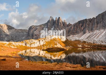 Acque cristalline del lago di Piani nel Parco Nazionale delle tre Cime di Laveredo, Dolomiti, Italia. Paesaggio pittoresco con montagne innevate, erba d'arancio e laghetto in autunno delle Alpi dolomitiche Foto Stock