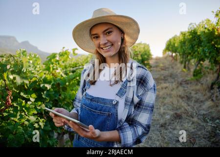 Giovani donne caucasiche felici in abbigliamento casual con tablet digitale accanto alle piante in fattoria Foto Stock