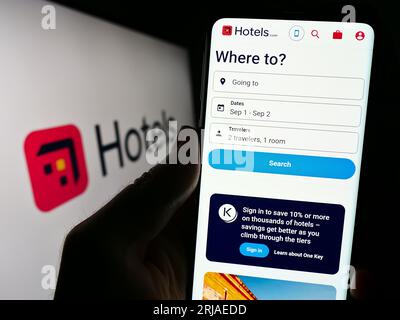 Person holding cellphone with webpage of US hotel booking company Hotels.com LP on screen in front of logo. Focus on center of phone display. Stock Photo