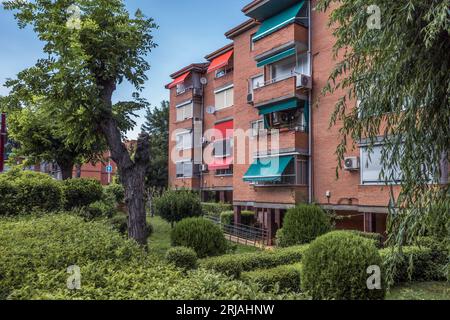 Nuovo edificio di appartamenti in mattoni rossi in un nuovo sviluppo con giardino, alberi, siepi, cespugli ed erba nella città di Guadalajara, Spagna, Europa Foto Stock