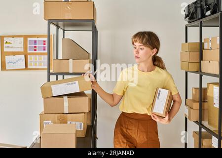 Giovane lavoratrice del mercato o del magazzino in attesa di un rack con pacchi imballati e alla ricerca di una scatola con il numero necessario Foto Stock