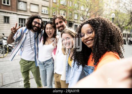 Gruppo multirazziale di amici che ridono e scattano un selfie per strada.allegro gruppo eterogeneo di giovani hipster che scattano una foto all'aperto e guardano Foto Stock