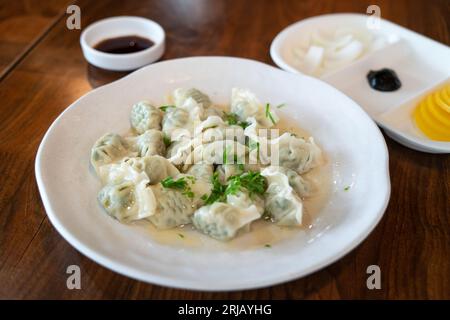 Gnocchi di erba cipollina freschi e deliziosi con cipolle verdi, jiaozi in piatto bianco su fondo di legno. Foto Stock
