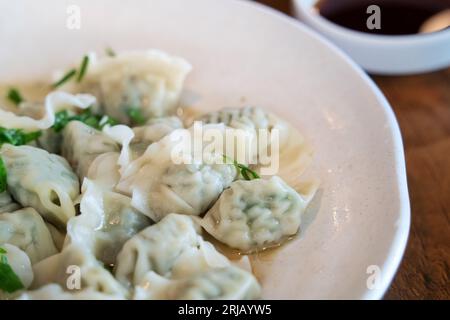 Gnocchi di erba cipollina freschi e deliziosi con cipolle verdi, jiaozi in piatto bianco su fondo di legno. Foto Stock